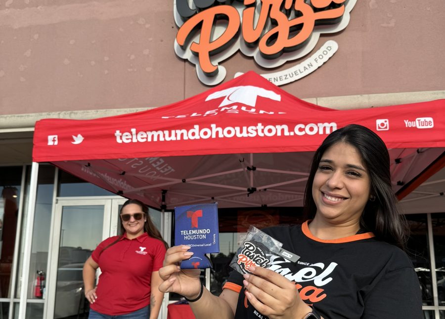 Promotora de Pastel Pizza con productos de Telemundo Houston bajo la carpa, frente al letrero de Pastel Pizza